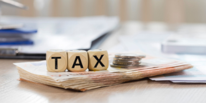 Wooden cubes spelling the word tax placed on top of money